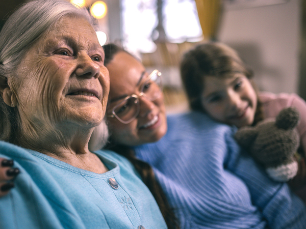 Three generations of a family, grandmother, mother and daughter, smiling together at home.